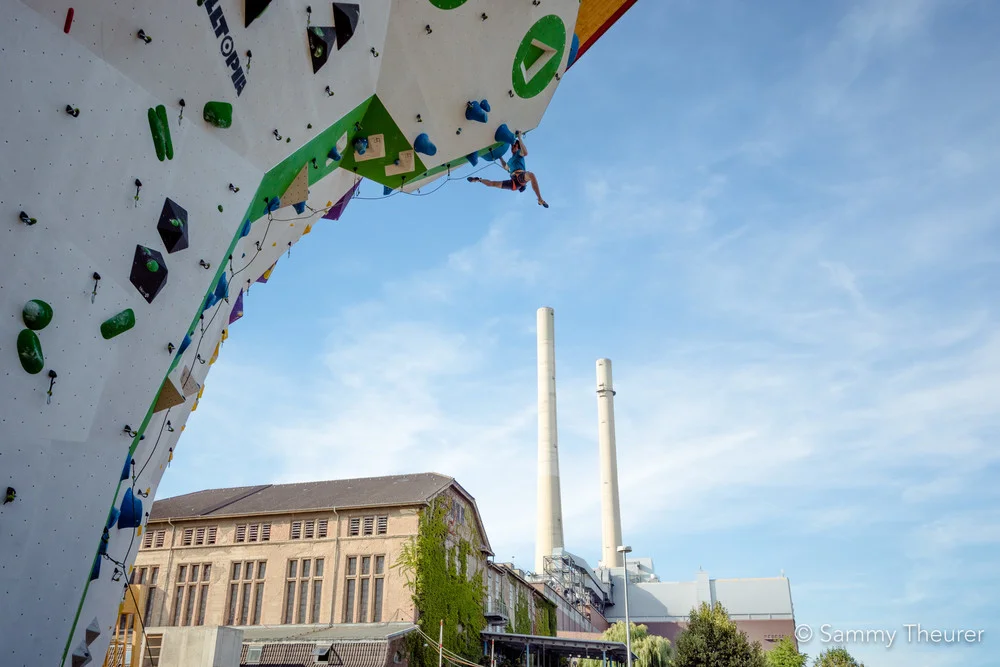 © Im Vordergrund Kletterer beim Seilklettern am Kletterturm im Außenbereich, im Hintergrund Kletterhalle © Im Vordergrund Kletterer beim Seilklettern am Kletterturm im Außenbereich, im Hintergrund Kletterhalle
