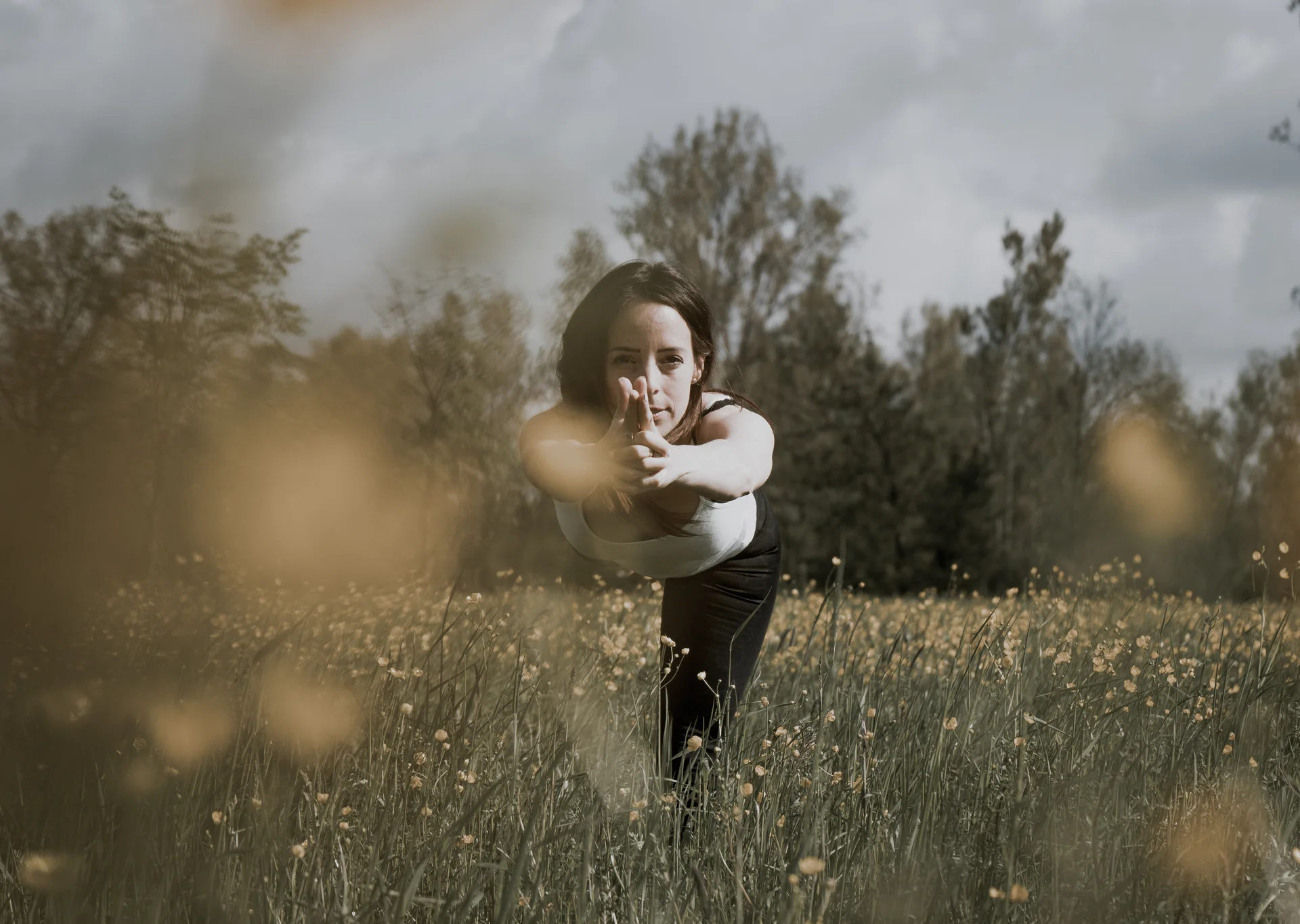 Frau macht Yoga auf einer Blumenwiese und blickt in die Kamera | © 2024 Verena Belzner